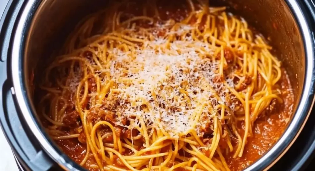 A stainless steel instant pot filled with freshly cooked instant pot spaghetti in a savory tomato-based sauce, topped with grated Parmesan cheese.