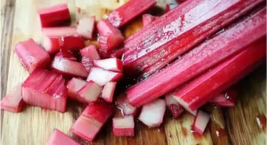 Fresh, vibrant red rhubarb stalks being chopped on a wooden cutting board, a key ingredient for a rhubarb cobbler recipe.
