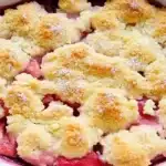 A freshly baked rhubarb cobbler in a white dish, featuring a golden crumble topping, part of a rhubarb cobbler recipe.