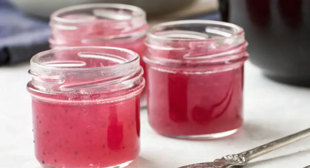 Three small glass jars filled with vibrant pink rhubarb jelly.