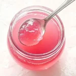 The Ultimate No-Fail Rhubarb Jelly Recipe (Perfect Set Every Time!) 18 Close-up top view of a spoonful of textured pink rhubarb jelly over a filled jar.