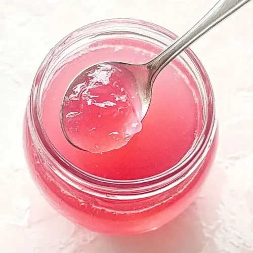 Close-up top view of a spoonful of textured pink rhubarb jelly over a filled jar.
