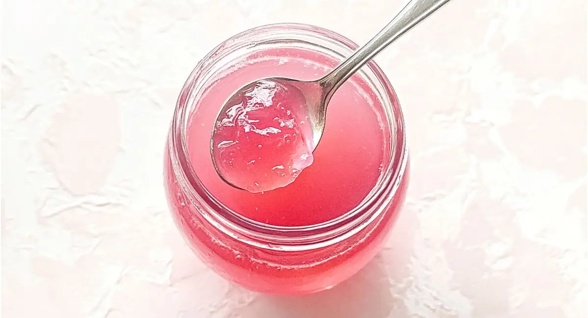 Close-up top view of a spoonful of textured pink rhubarb jelly over a filled jar.
