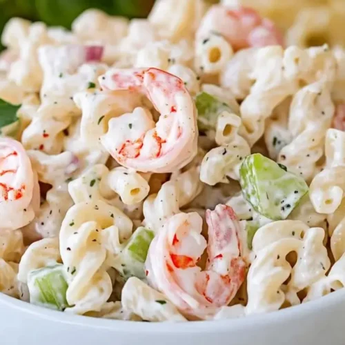 Creamy shrimp pasta salad recipe with elbow macaroni, shrimp, celery, and red onion in a white bowl.